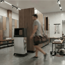 Load image into Gallery viewer, HLS24DPO stainless steel trash can with  caster wheels in a modern gym locker room.